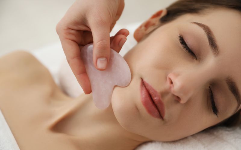 A close-up of a client receiving a rose quartz Gua Sha facial massage along the jawline by a professional Lumi Glow therapist in Bangkok.