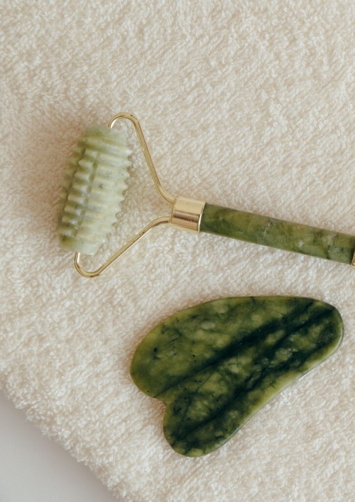 A green jade textured face roller and jade Gua Sha tool resting on a white towel, showcasing the holistic skincare instruments used by Lumi Glow Bangkok.
